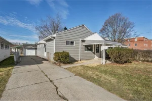 Single-story gray home with driveway, front yard, and covered porch entry under clear blue sky