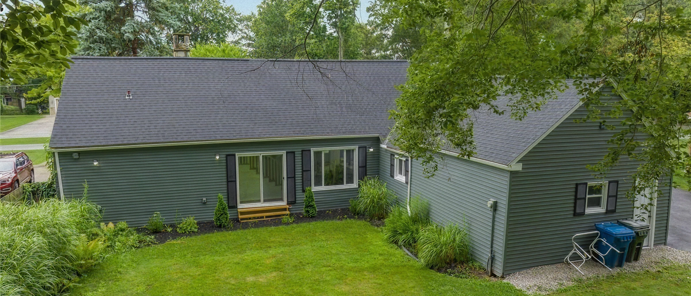 Wide-angle photo of a green siding single-family home with backyard and landscaping